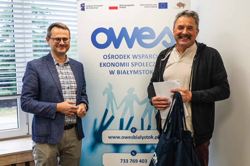 Dwaj uśmiechnięci mężczyźni stoją na tle rollupu z logo OWES.