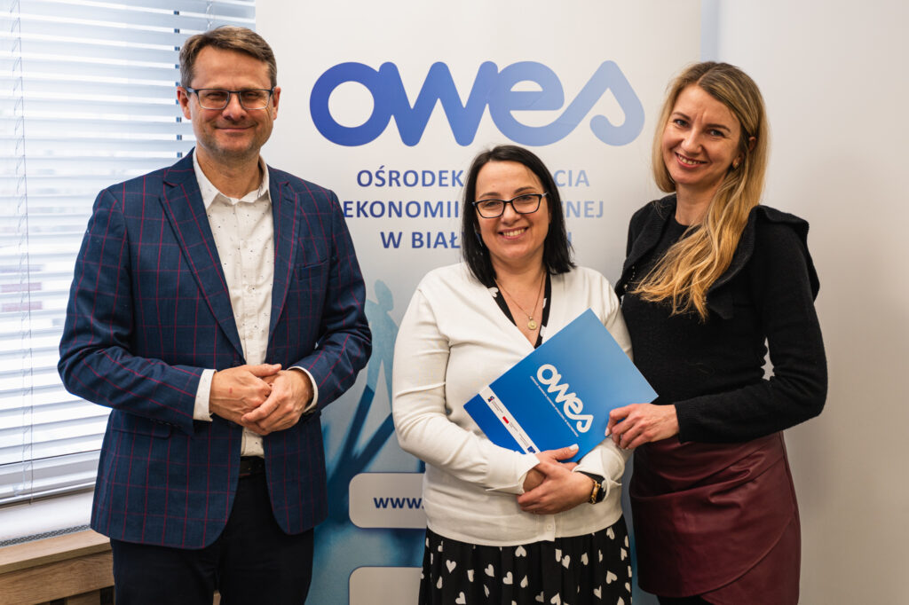 Dwie kobiety i mężczyzna stoją z teczką, w której jest umowa o dofinansowanie