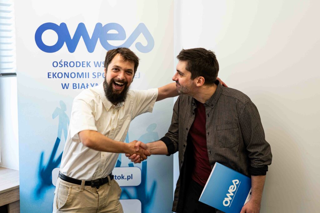 Dwóch roześmianych mężczyzn podaje sobie ręce w geście gratulacji.