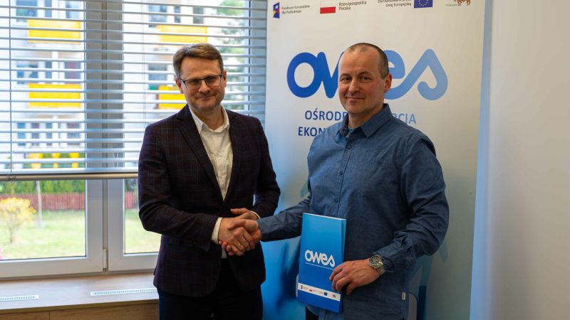 Dwóch uśmiechniętych mężczyzn w średnim wieku podaje sobie ręce.