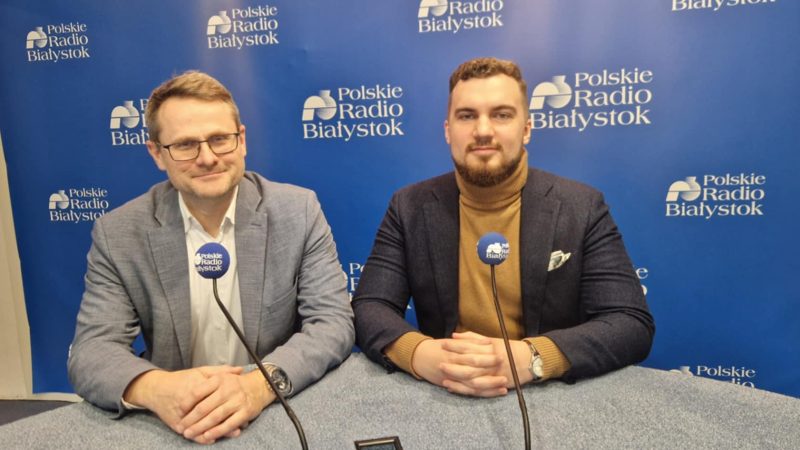 Dwóch mężczyzn siedzi przy stole. Przed nimi stoją mikrofony.