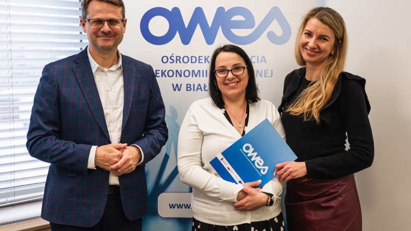 Dwie kobiety i mężczyzna stoją z teczką, w której jest umowa o dofinansowanie