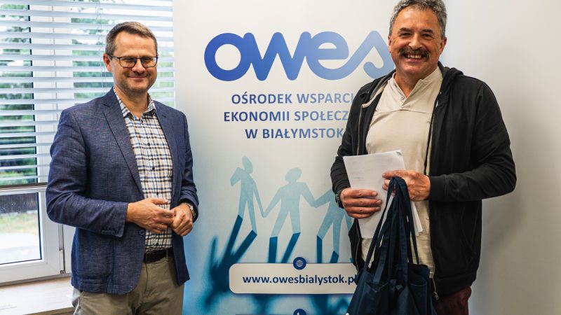 Dwaj uśmiechnięci mężczyźni stoją na tle rollupu z logo OWES.